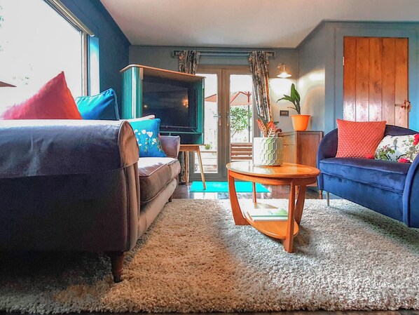 A living room with a sofa, a television, a coffee table, and a door leading outside.