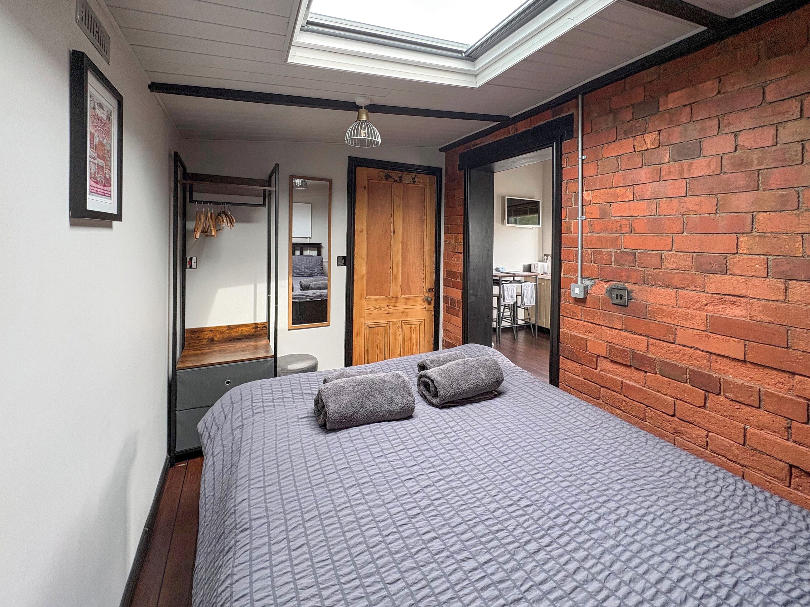 Un dormitorio con tragaluz, una cama con almohadas, una puerta de madera y una pared de ladrillo.