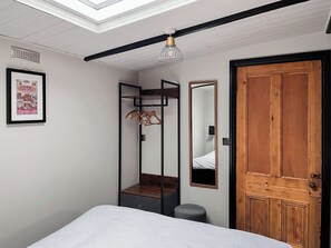 A bedroom with a bed, a wooden door, a mirror, a hanging light fixture, and a framed picture on the wall.