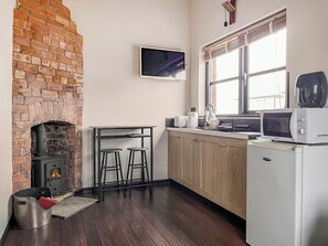 Una cocina con chimenea de ladrillo, armarios de madera, microondas y ventana con persianas.
