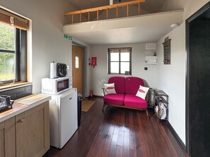 Una cocina compacta con microondas, tostadora y refrigerador pequeño, un sofá rojo con cojines, una ventana y señal de salida de incendios.