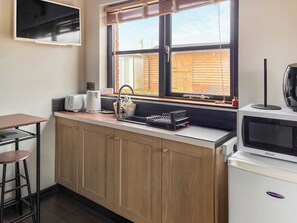 A compact kitchen with wooden cabinets, a sink, a toaster, a kettle, and a microwave.