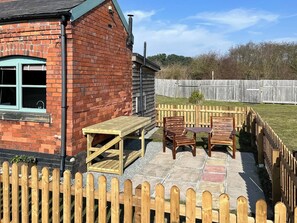 A brick house with a patio, wooden table, and chairs.