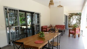 Un comedor con una mesa y sillas de madera, un sofá rojo estampado y vistas a la vegetación exterior.