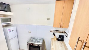 Een kleine keuken met een gasfornuis, een magnetron en een kleine koelkast.