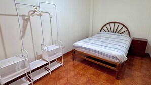 Een slaapkamer met een houten bed, een witte metalen plankkast en een betegelde vloer.