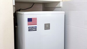 Een witte koelkast met een sticker van de skyline van Manhattan en een Amerikaanse vlag, en erboven een witte magnetron.