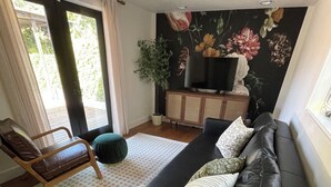 A modern living room with a black sofa, a wooden chair, a small round table, and a large window with curtains. - Curtis Park Charmer! (Sacramento)