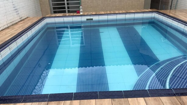 Une piscine rectangulaire à l’eau d’un bleu limpide, entourée d’une terrasse en bois et bordée de murs carrelés.