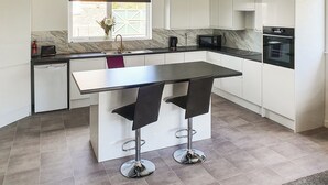 A modern kitchen with white cabinets, a black countertop, a built-in oven, and a window with a view of greenery. - Classroom One - UK48650 (Lifton)