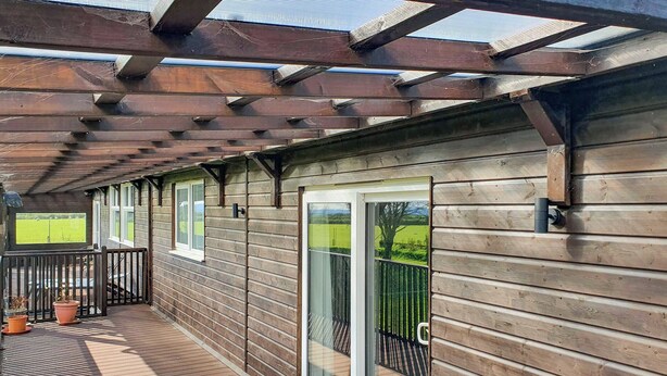 A wooden deck with a pergola, sliding glass doors, and potted plants. - Classroom One - UK48650 (Lifton)