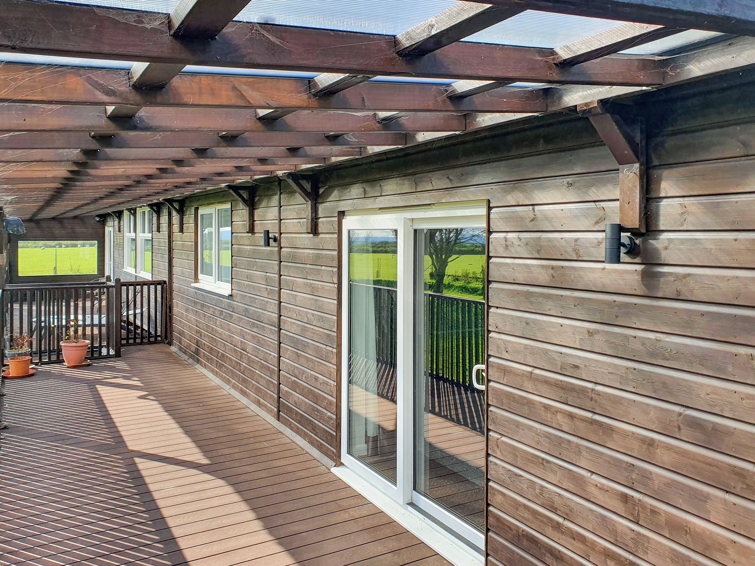 A wooden deck with a pergola, sliding glass doors, and potted plants.