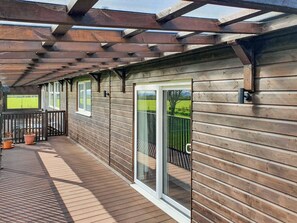 Eine Holzterrasse mit einer Pergola, Schiebetüren und Kübelpflanzen.
