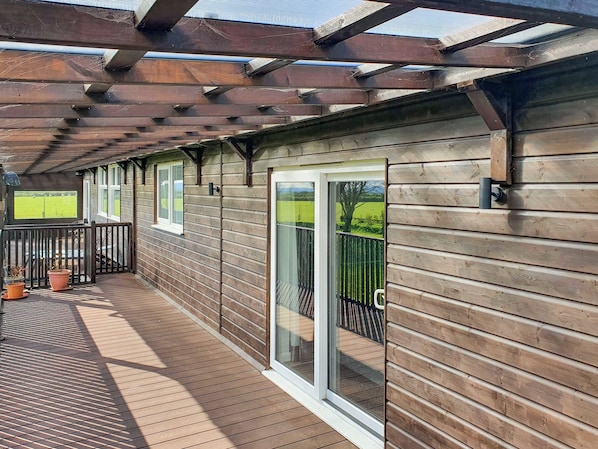 A wooden deck with a pergola, sliding glass doors, and potted plants.