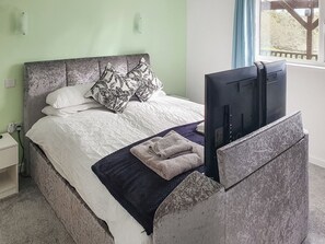 A bed with a grey headboard, white bedding, and a black and white patterned pillow. A flat-screen TV is mounted on the headboard.