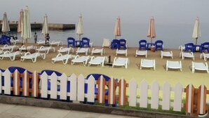 Zona de playa con hileras de sillas reclinables blancas y sillas azules, algunas con sombrillas.