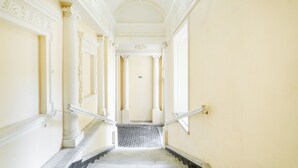 A grand hallway with a marble staircase, white columns, and a chandelier.
