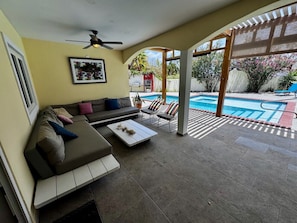 Un patio techado con un sofá, sillas y una piscina.