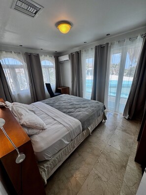 A bedroom with a bed, a desk, a chair, and a view of a pool.