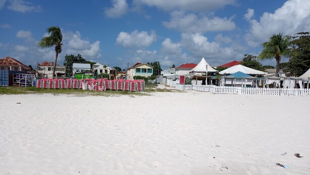 Une plage de sable blanc, une clôture blanche et, au loin, des bâtiments aux toits rouges.