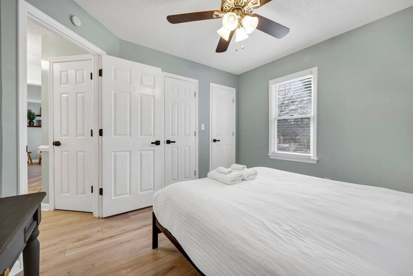 Une chambre à coucher avec un lit, des portes blanches, un ventilateur de plafond et une fenêtre avec des stores.