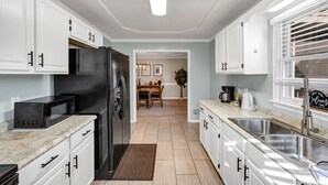 A modern kitchen with white cabinets, a black refrigerator, a microwave, and a sink. - Sawgrass Cottage | 3BR with Deck (Columbia)