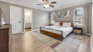 A bedroom with a bed, a ceiling fan, a window with curtains, and a door leading to a bathroom. - Sawgrass Cottage | 3BR with Deck (Columbia)