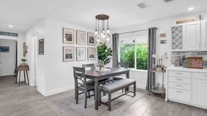 Une cuisine moderne avec des meubles blancs, un coin repas doté d’une table et de chaises en bois, et une grande fenêtre offrant une vue sur la verdure.