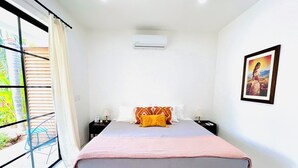 Une chambre à coucher comprenant un lit, une table de chevet, un climatiseur fixé au mur et une fenêtre avec des rideaux.