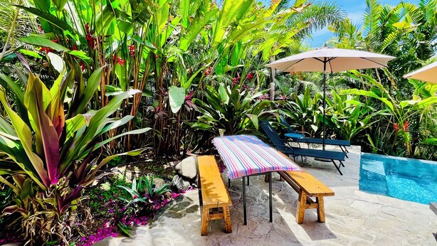Un espace aménagé au bord de la piscine, avec une terrasse en pierre, des chaises longues en bois et une table à rayures.