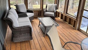 Un espace extérieur aménagé, abrité et doté de mobilier en osier et d’une table en verre, le tout entouré de grandes fenêtres.