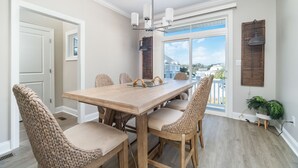 Un coin repas avec une table en bois et des chaises en osier, un ventilateur de plafond et une vue sur l’extérieur.