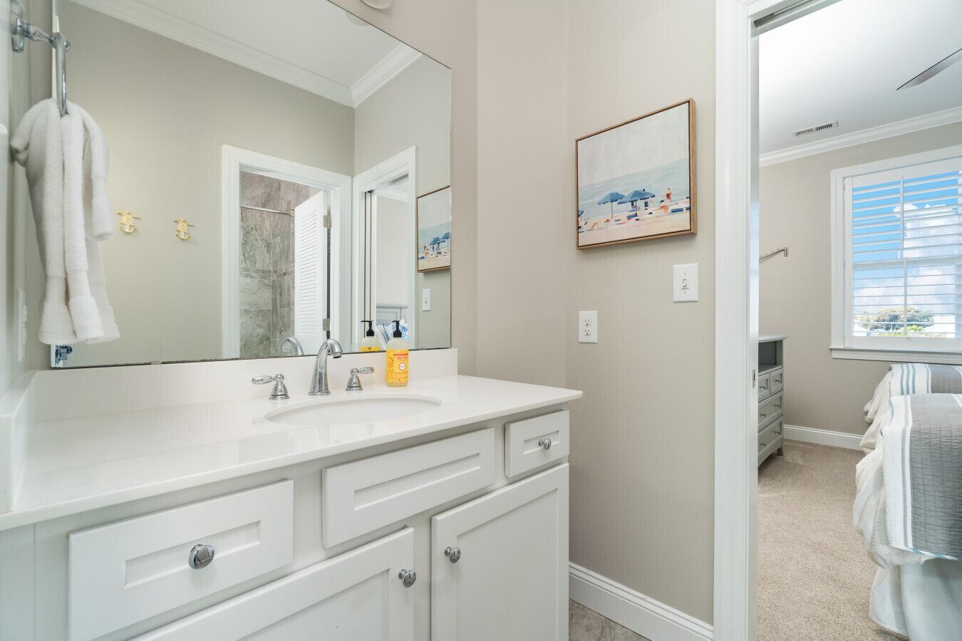A bathroom with a large mirror, white vanity, and a framed beach picture on the wall.