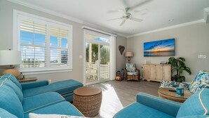 Un salon spacieux avec un grand canapé bleu, un ventilateur de plafond et une vue sur l’extérieur grâce à de grandes portes-fenêtres coulissantes.