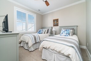 Quarto com duas camas, uma escrivaninha, televisão e ventilador de teto.