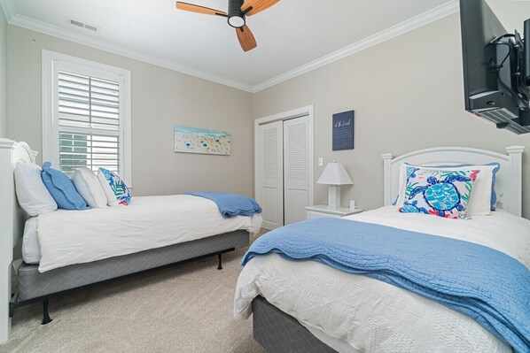 A bedroom with two beds, a ceiling fan, a TV, and a beach-themed artwork.