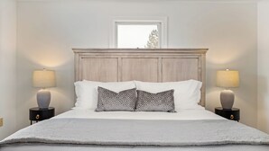 Een net opgemaakt bed met een houten hoofdbord, twee bedlampen en een raam erboven.