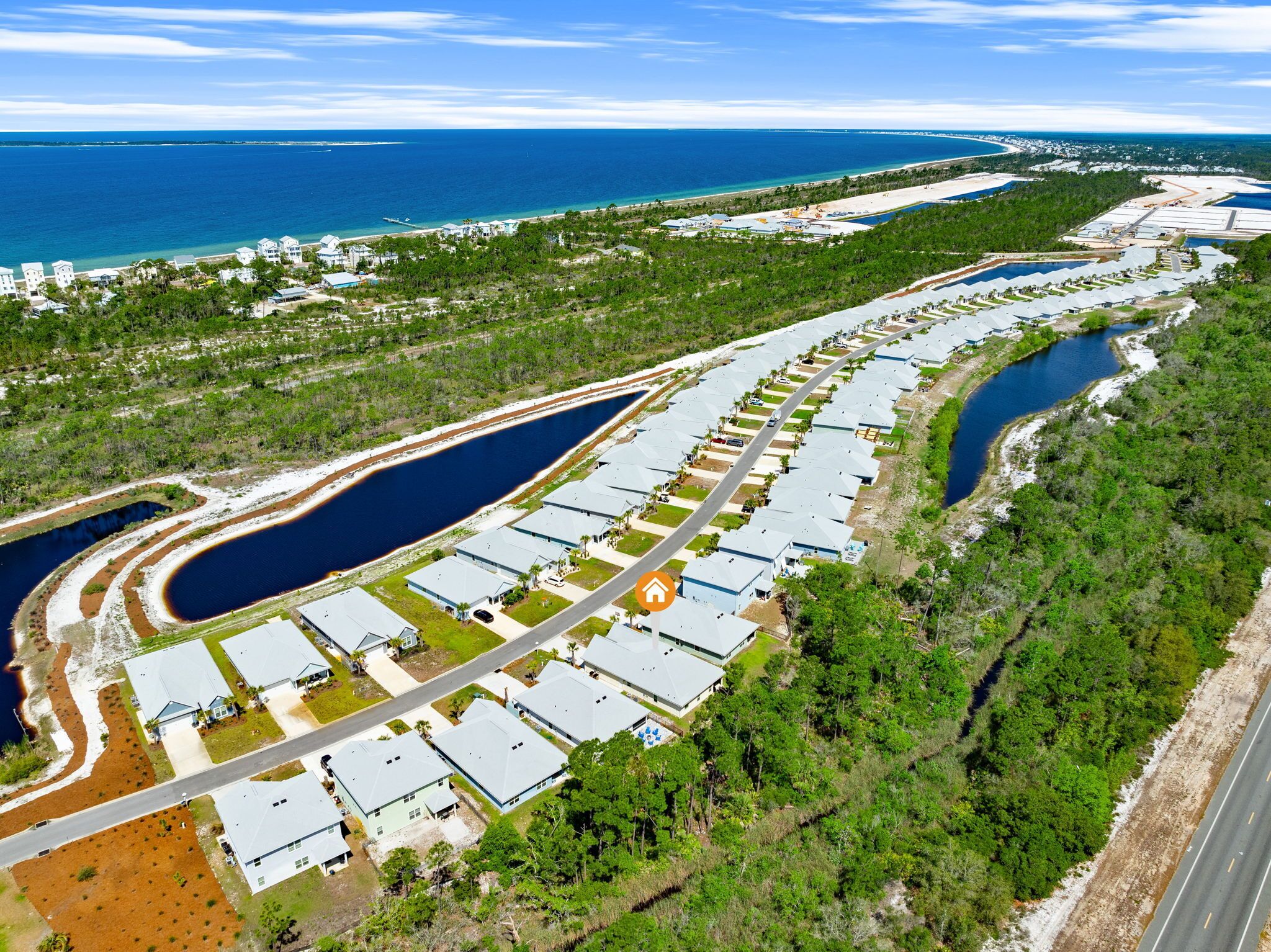 Vue aérienne d’une zone résidentielle côtière, avec des maisons, une route et une voie navigable.