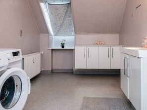 A laundry room with a washing machine, a drying rack, a small window with a curtain, and a countertop with a potted plant. - 6 Person Holiday Home in Ringkobing (Ringkobing)