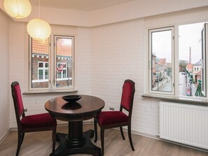 A dining area with a round table, two chairs, a window with a view of buildings, and a white brick wall.