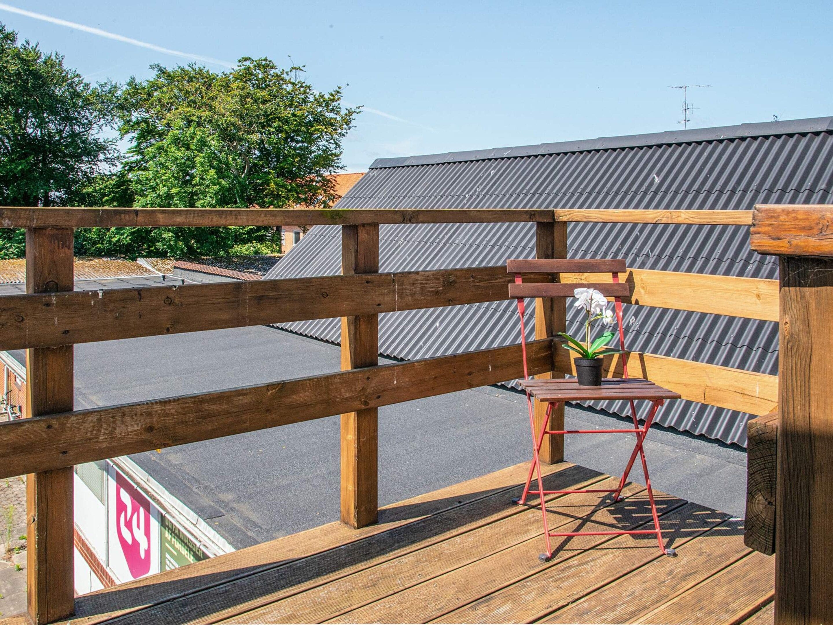 Una terraza de madera con una silla plegable roja y una planta en maceta.