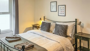 Ein ordentlich bezogenes Bett mit Kissen, ein Nachttisch mit Lampe und zwei gerahmte Bilder an der Wand.