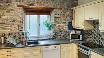 A kitchen with stone walls, a window, a sink, a microwave, and cabinets.