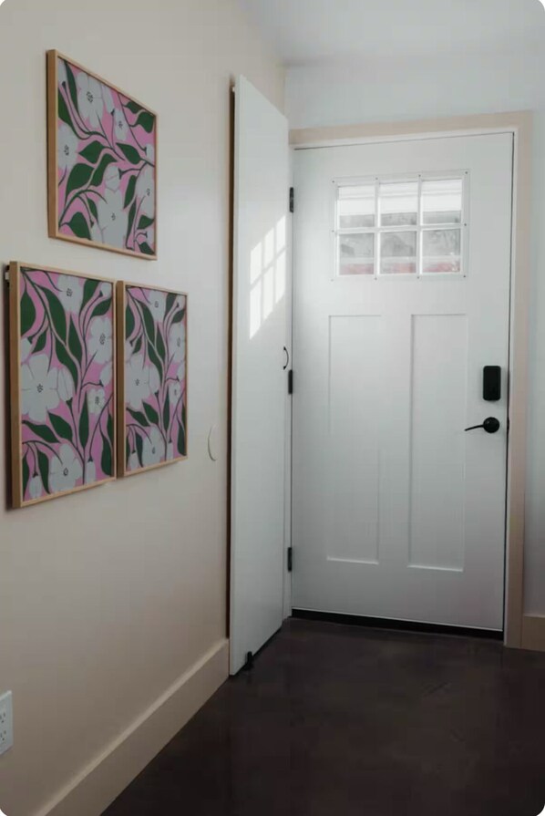 Ein Flur mit einer weißen Tür, einem Fenster mit geätztem Glas und drei gerahmten floralen Kunstwerken an der Wand.