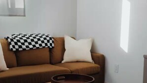 A living room with a brown sofa, a small ottoman, and a checkered throw blanket. - Charming 1-bedroom house with AC and WiFi in Whittier (Whittier)