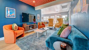 A modern living room with a blue wall, orange armchairs, a blue sofa, and a wooden coffee table. - Magical Stay Near Disneyland with Pool & Fire Pit (Santa Ana)