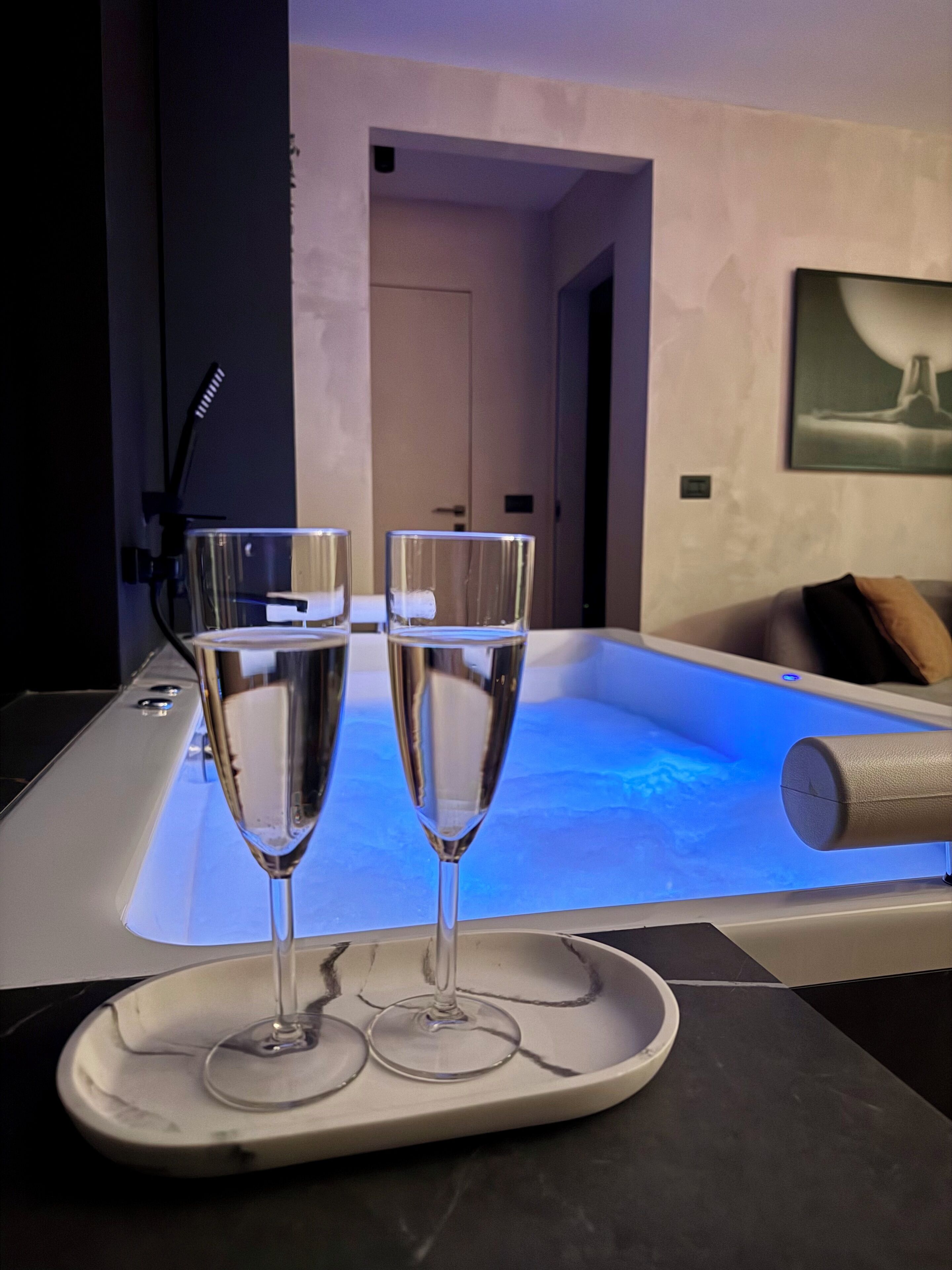 A modern bathroom with a heated bathtub, a tray with two champagne flutes, and a towel rack.