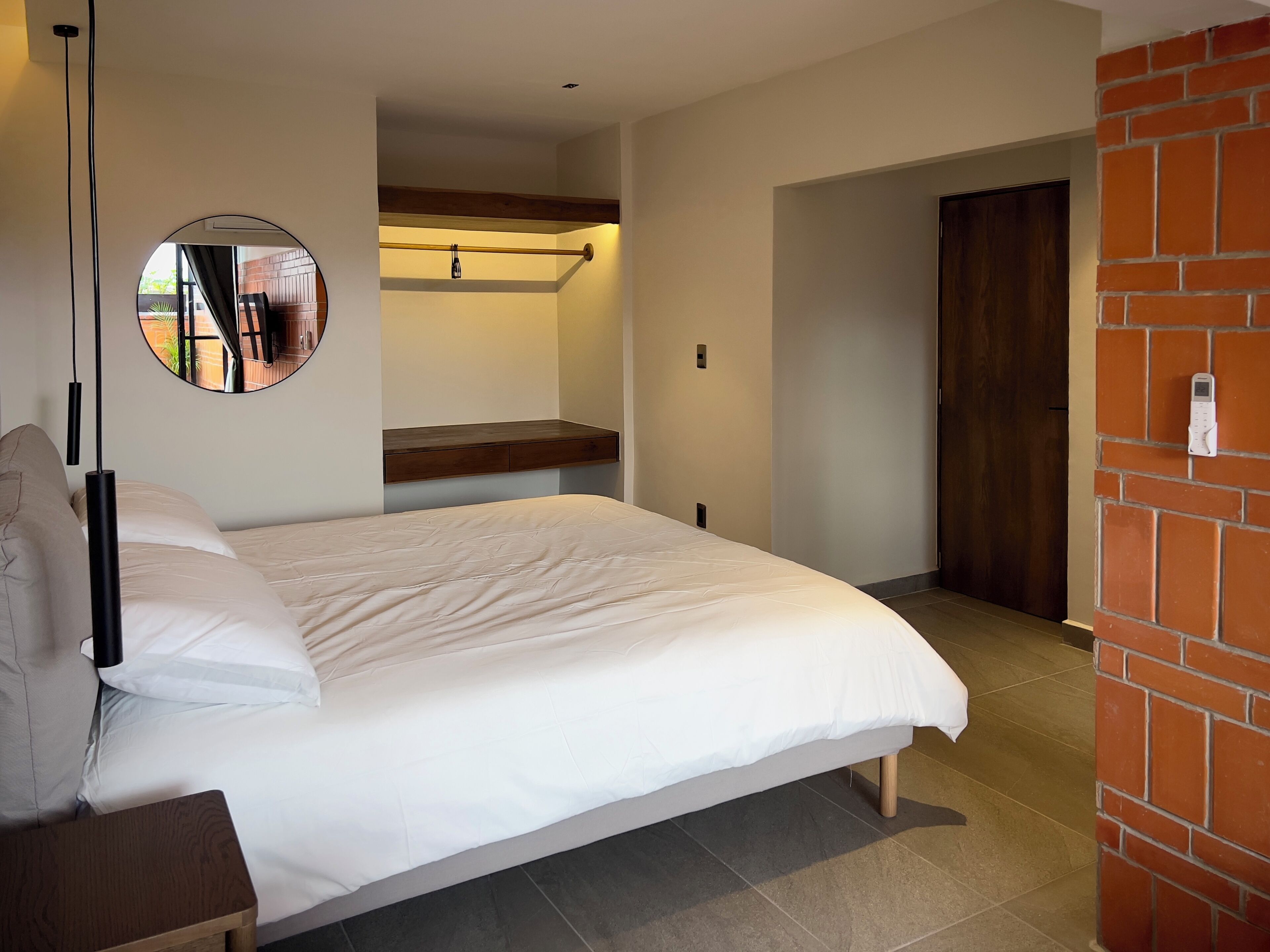 A bedroom with a bed, a bedside table, a mirror, and a brick wall.