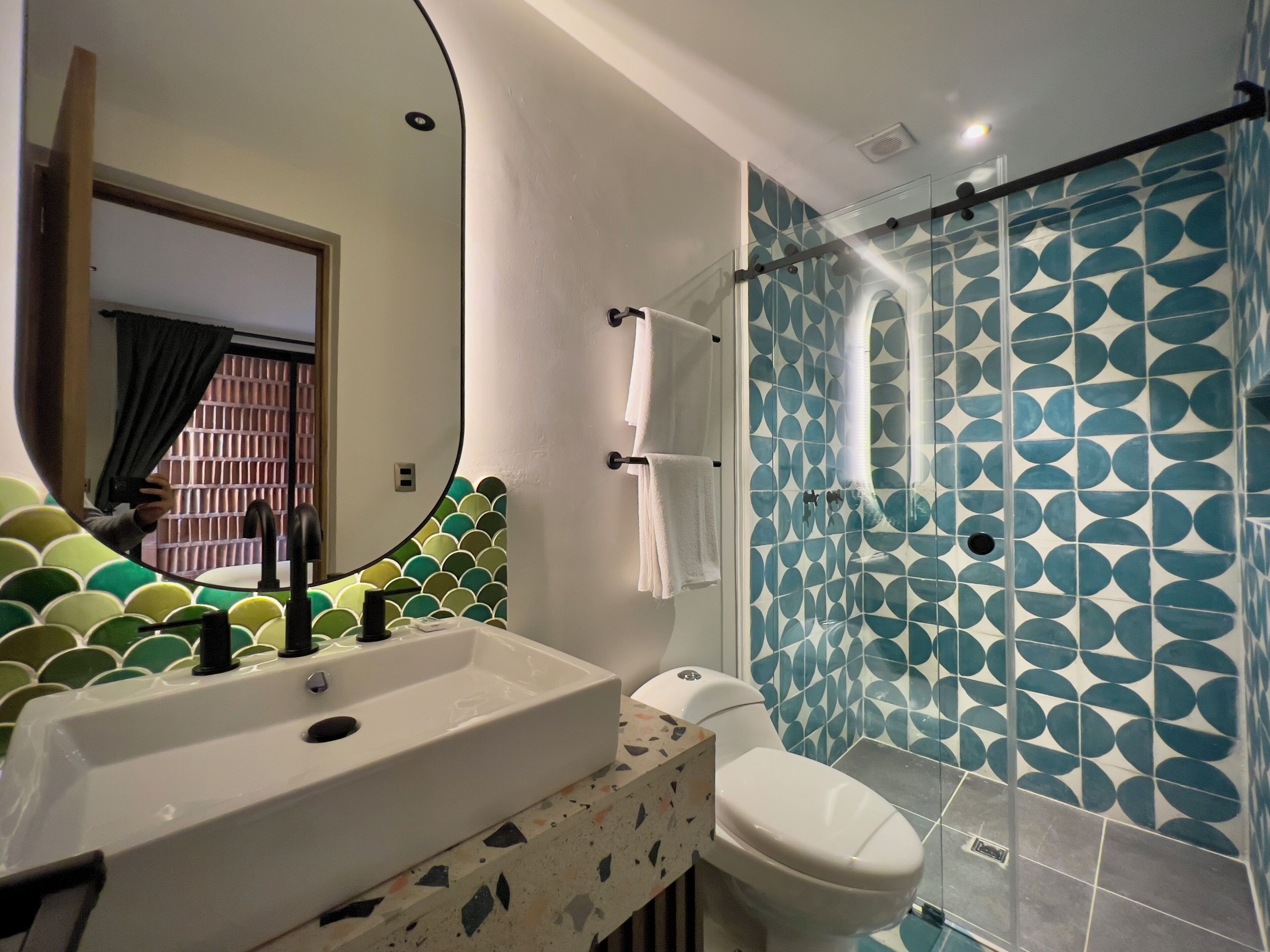 Ein Badezimmer mit einem weißen Waschbecken, einer Toilette und einer Dusche mit blauen, gemusterten Fliesen.