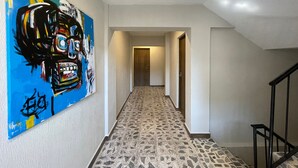 Ein Flur mit einem farbenfrohen abstrakten Gemälde an der linken Wand, einem gemusterten Boden und einer Treppe auf der rechten Seite.